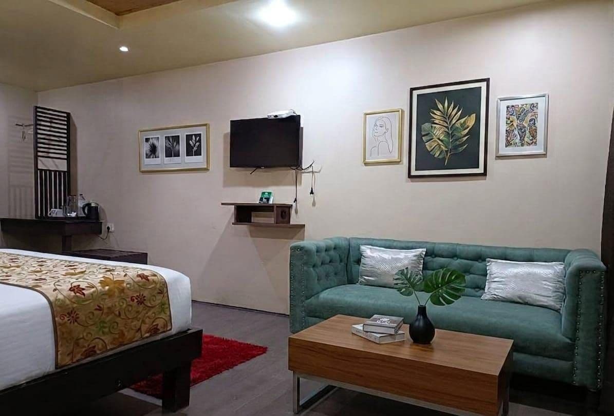 Una habitación de hotel con una cama, un sofá verde, una mesita de centro y un televisor montado en la pared.