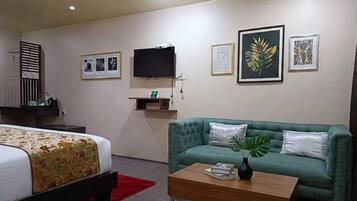 Una habitación de hotel con una cama, un sofá verde, una mesita de centro y un televisor montado en la pared.