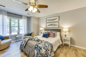 A bedroom with a bed, two bedside tables, a chair, a ceiling fan, and two framed pictures on the wall.