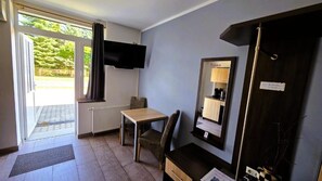 A room with a bed, a desk, a chair, a television mounted on the wall, and a window with curtains.