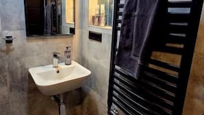 Un baño moderno con lavamanos, espejo, toallero y paredes con azulejos.