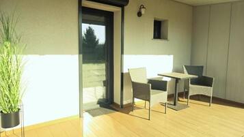 A balcony with a wooden floor, two wicker chairs, a small table, and a potted plant.