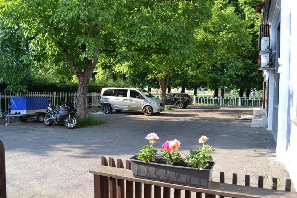 Ein Parkplatz mit einem Auto und einem Motorrad, umgeben von Bäumen und einem Zaun.