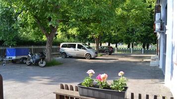 Ein Parkplatz mit einem Auto und einem Motorrad, umgeben von Bäumen und einem Zaun.