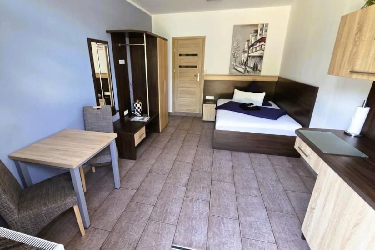 A compact room with a bed, a desk, a chair, a wardrobe, and a small table.