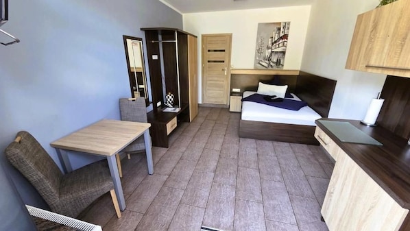 A compact room with a bed, a desk, a chair, a wardrobe, and a small table.