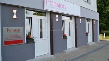 A building with a sign reading 'Pension Schwarze Pumpe' and a smaller sign below it with contact information.