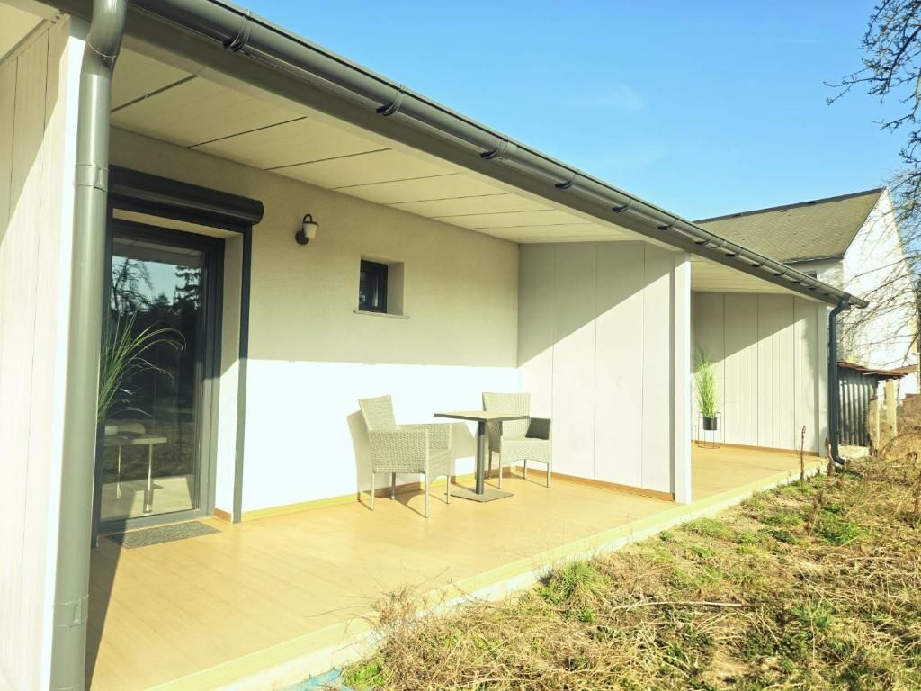 A modern house with a covered patio, a sliding glass door, and a small table with chairs.