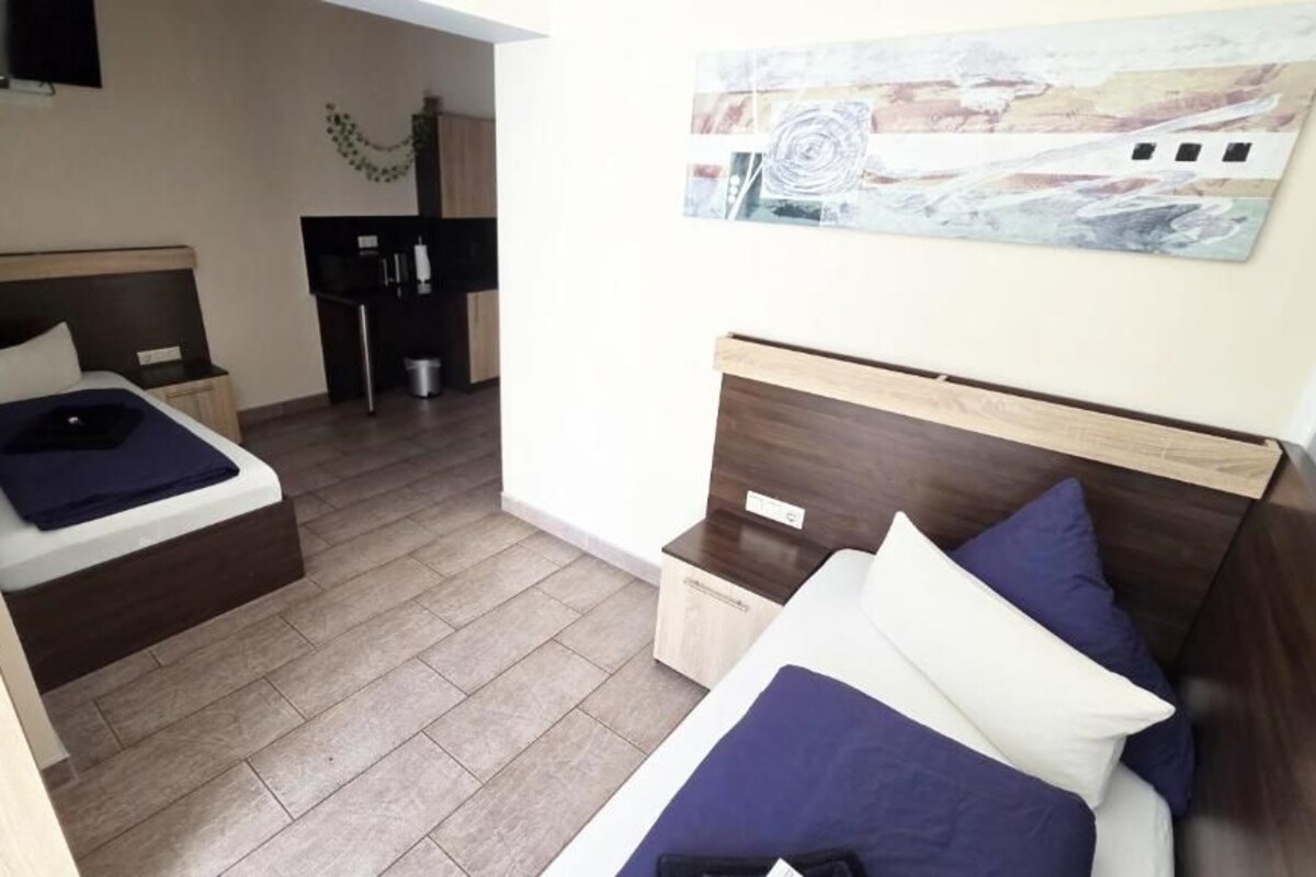 A hotel room with two beds, a small desk, a television, and a painting on the wall.
