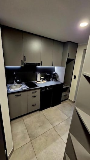A compact kitchen with grey cabinets, a black countertop, and a dishwasher.