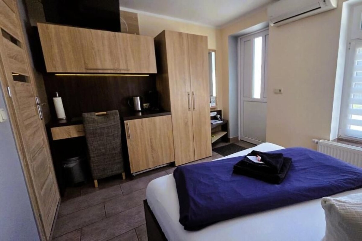 A compact room with a bed, a kitchenette, and a window.