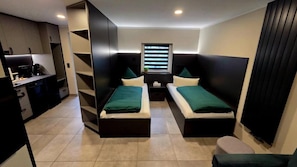 A compact room with two single beds, a small kitchenette, and a window with blinds. - Pension Schwarze Pumpe (Spremberg)