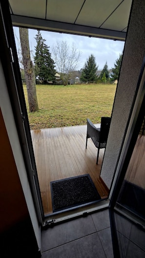 A doorway leading to an outdoor area with a wooden deck, a black chair, and a doormat.