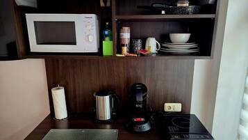 A kitchenette with a microwave, coffee maker, kettle, and a small countertop.