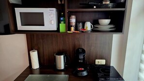A kitchenette with a microwave, coffee maker, kettle, and a small countertop.