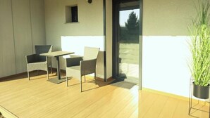 Un balcón con una mesa, dos sillas, una planta en maceta y una puerta que da al exterior.