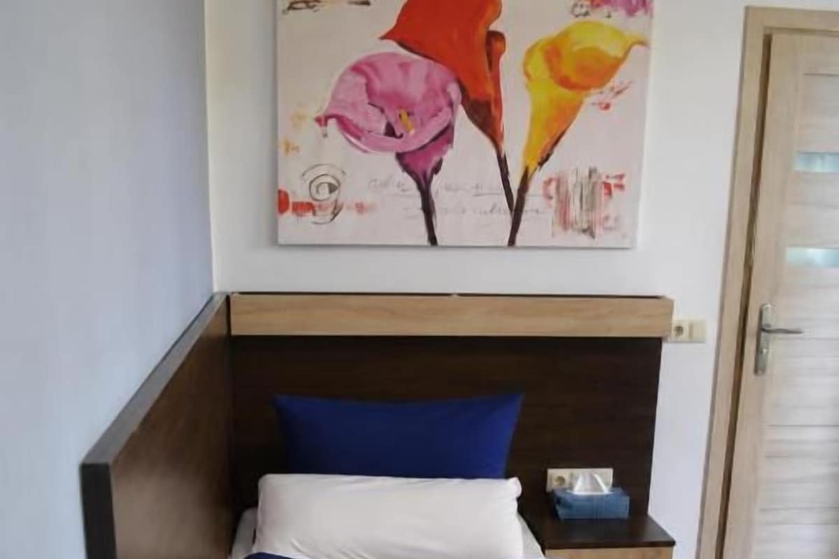 A single bed with a blue blanket, a pillow, and a small table with a lamp beside it.