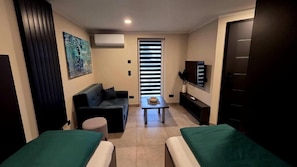 Un espacio habitable compacto con sofá, una mesita, un televisor y una puerta.