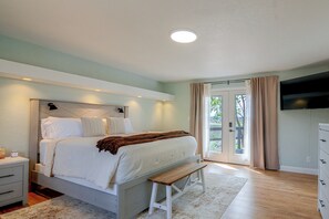A bedroom with a bed, bedside tables, a bench, a TV, and a view through the door. - Red Rock Retreat in Kanab | Epic Views | Near Zion (Kanab)