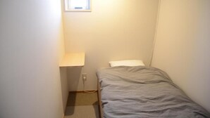 A small, narrow room with a single bed, a window, and a wall-mounted light fixture. - saino tsuno guesthouse (uedashi chuuou)