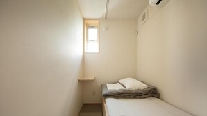 A small, narrow room with a single bed, a window, and a wall-mounted shelf. - saino tsuno guesthouse (uedashi chuuou)