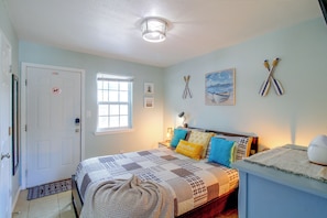 A bedroom with a bed, a bedside table, a lamp, a window, and a door. - Corner Cottage - Just Minutes from the Water (Aransas Pass)