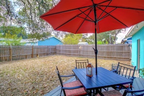 A patio with a table and chairs, a red umbrella, and a wooden fence. - Corner Cottage - Just Minutes from the Water (Aransas Pass)