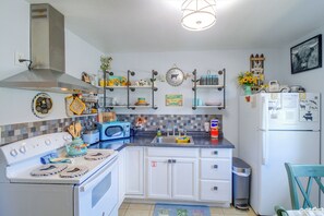 Una cocina con armarios blancos, estufa, microondas y refrigerador. Hay objetos decorativos en los estantes y un cartel de bienvenida.