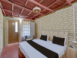 A bedroom with a brick wall, a wooden ceiling, a bed with white and black bedding, a bedside table, and a mirror.