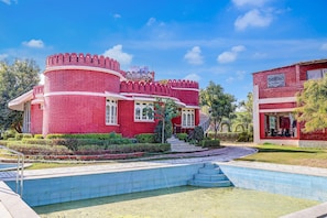 A red brick building with a circular tower, a swimming pool, and a well-maintained garden.