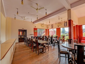 A spacious dining area with multiple tables and chairs, ceiling fans, and large windows allowing natural light.