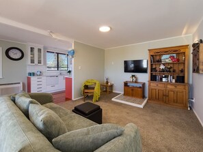 Ein Wohnzimmer mit einer Couch, einem Fernseher, einem Holzschrank und einer Küchenzeile mit Schränken und einem Fenster.