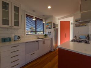 A modern kitchen with white cabinetry, a stainless steel refrigerator, and a red accent wall. - Coastal Rhythm - Haumoana (Haumoana)