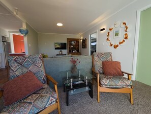 Ein Wohnzimmer mit zwei gemusterten Sessel, einem Glastisch und einem Sofa.