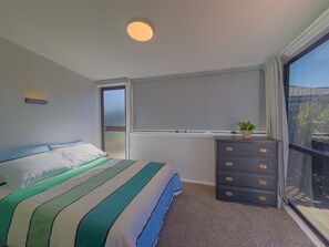 Ein Schlafzimmer mit Bett, Kommode, Fenster und Deckenleuchte.