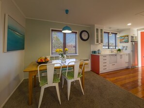 A modern kitchen with a dining table, chairs, a clock, and a window with blinds. - Coastal Rhythm - Haumoana (Haumoana)