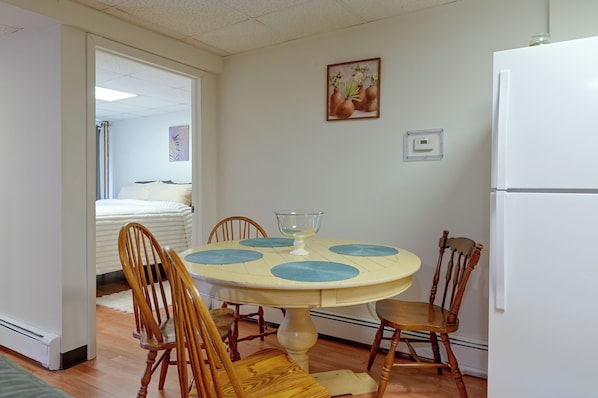 Un comedor con una mesa redonda, cuatro sillas y un refrigerador blanco.
