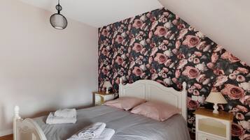 A bedroom with a sloped ceiling, a bed with white bedding, two bedside tables with lamps, and a floral wallpaper.