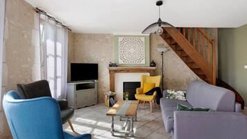 A living room with a TV, seating, a fireplace, and a staircase.