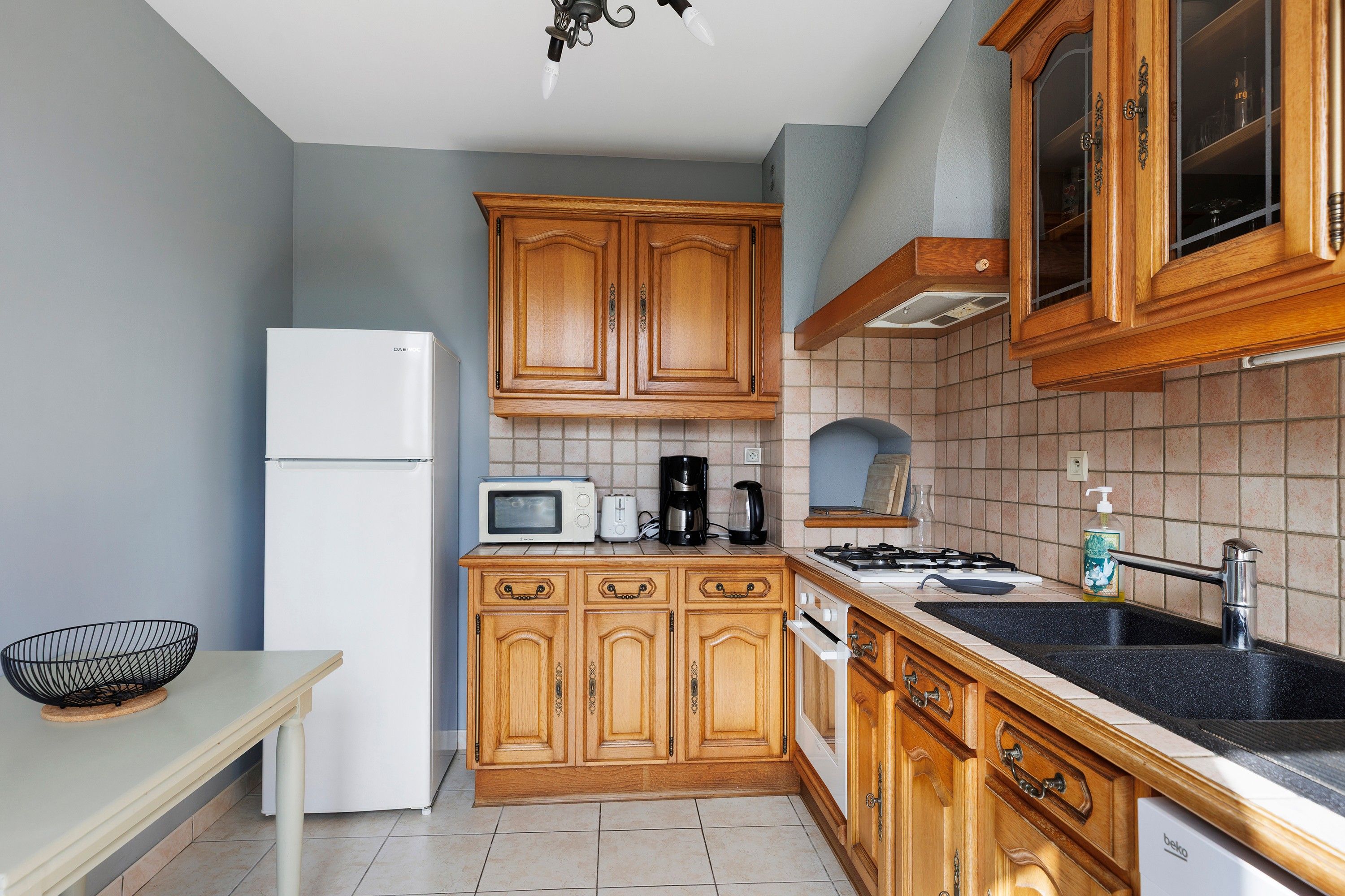 A kitchen with wooden cabinets, a white refrigerator, a microwave, a coffee maker, and a sink.
