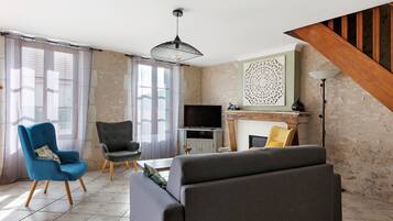 Een woonkamer met een bank, stoelen, een televisie en een open haard.