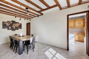 A dining area with a wooden table and chairs, a world map on the wall, and a kitchen visible through an open doorway.