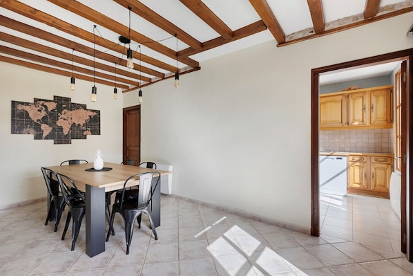 Un comedor con mesa y sillas de madera, un mapa del mundo en la pared, y una cocina visible a través de un vano abierto.