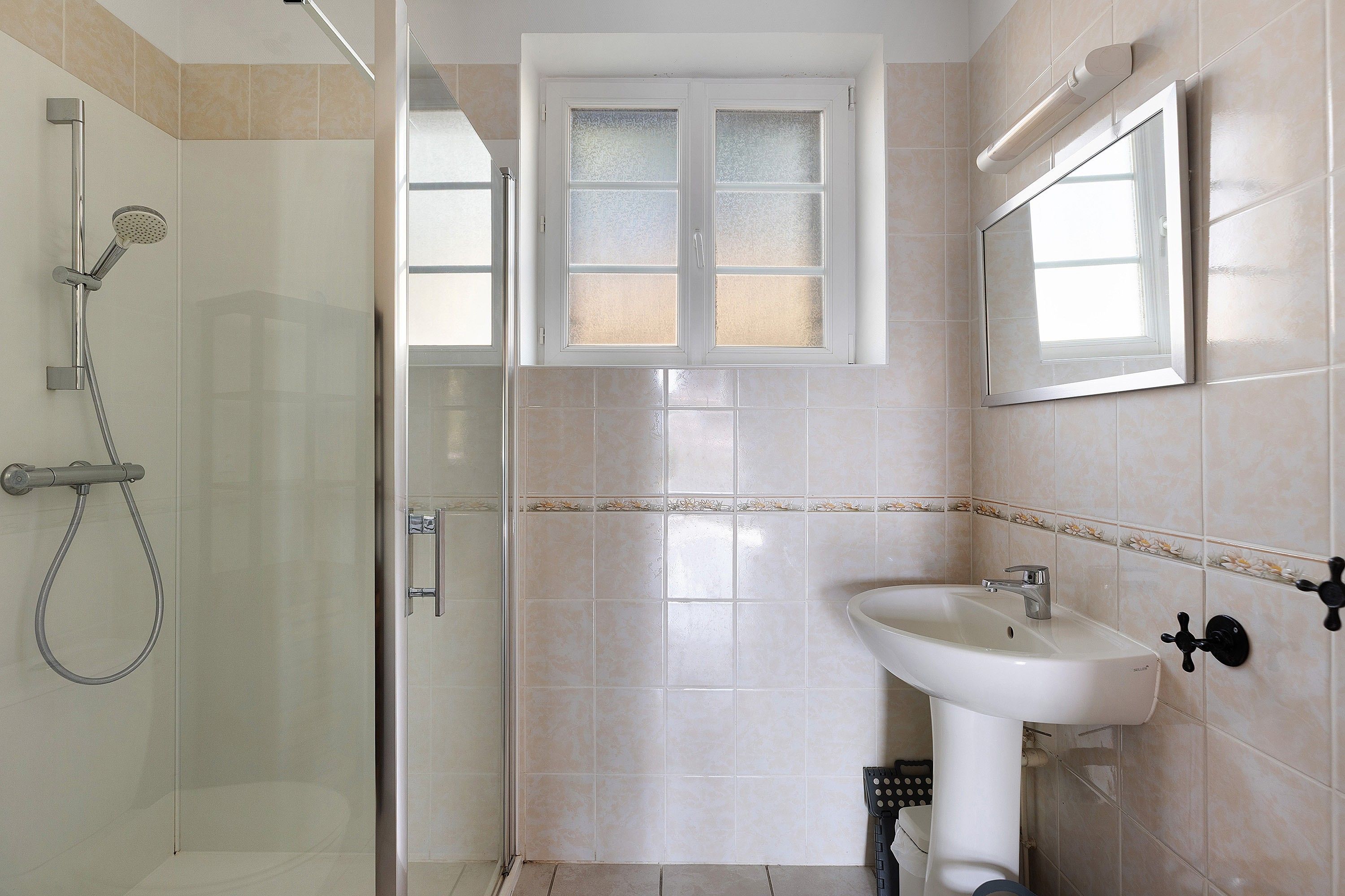 Une salle de bain avec une douche, un lavabo et une fenêtre.