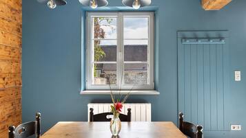 A room with a wooden table, chairs, a vase with flowers, a window with a view, and a radiator.
