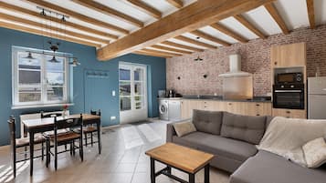 Una cocina moderna con pared de ladrillo, vigas de madera y zona de comedor con mesa y sillas.