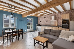 Une cuisine moderne avec un mur en briques, des poutres en bois et un coin repas comprenant une table et des chaises.