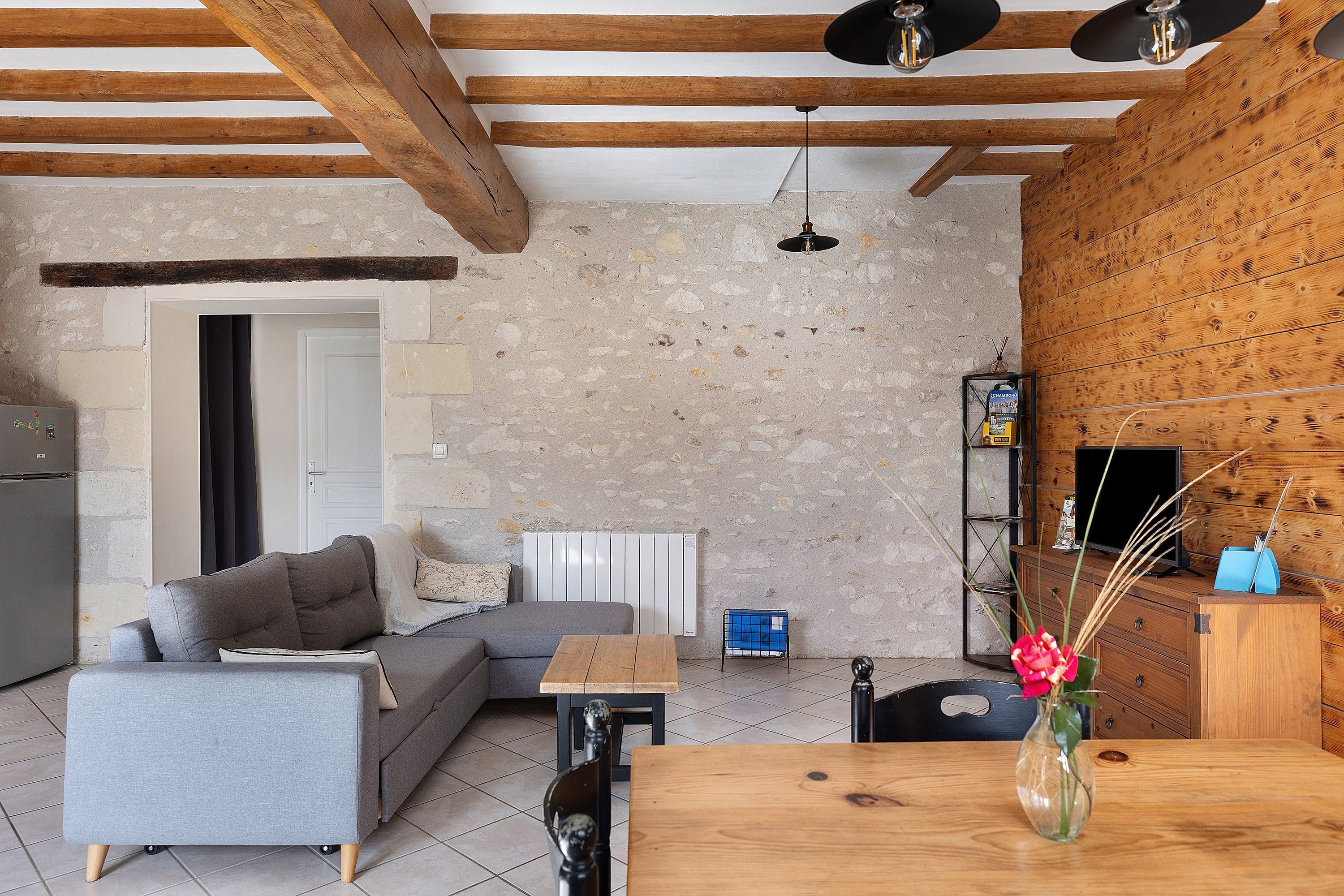 A living room with a grey sofa, a wooden dining table, and a stone wall.