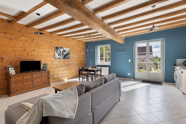 A living room with a sofa, a TV, wooden beams, and a dining area with a table and chairs.
