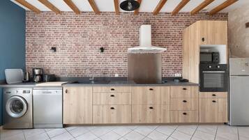 Une cuisine avec un mur en briques, des meubles en bois, un four encastré et un lave-linge.